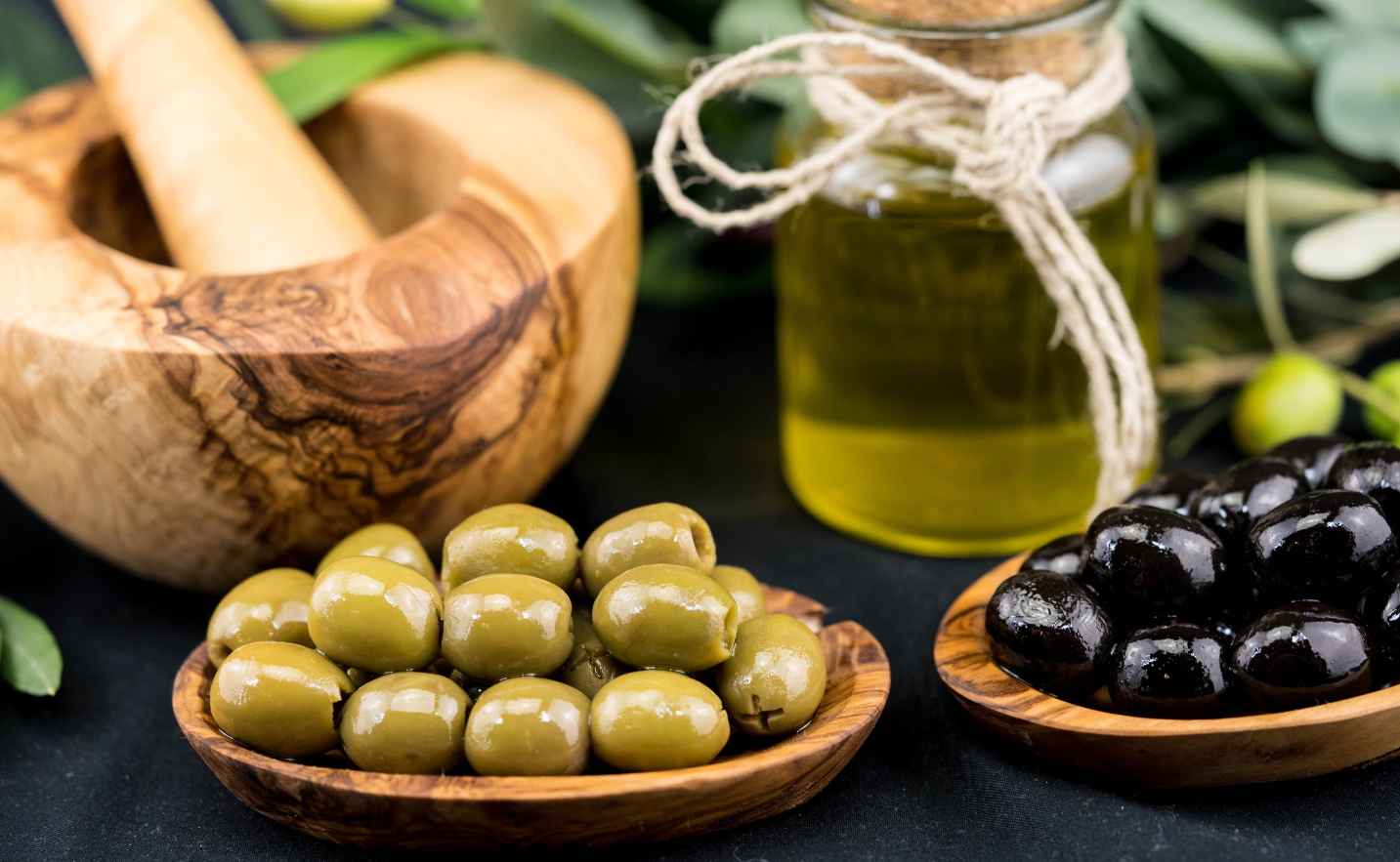 Green and black olives in wooden bowls with olive oil in the background