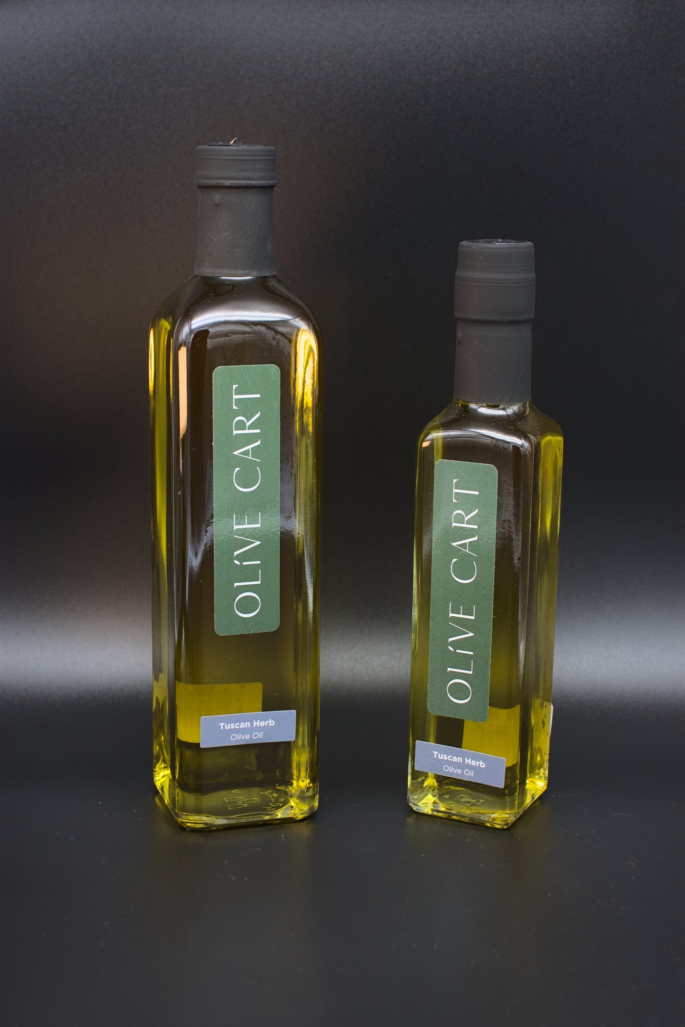 Two different sized bottles of Olive Cart's garlic lemon olive oil with lemons and garlic cloves