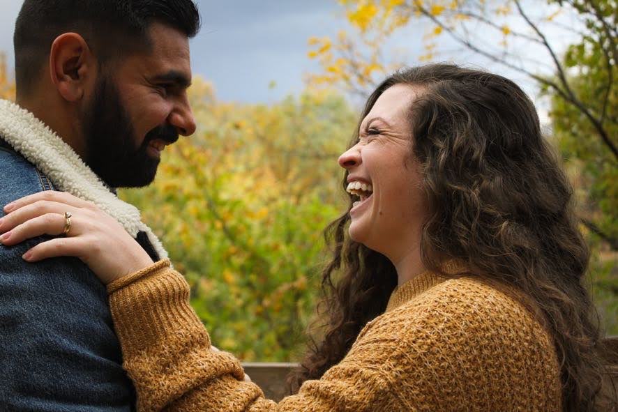 Owners, Ellie & Saša, laughing together outdoors with fall foliage in the background