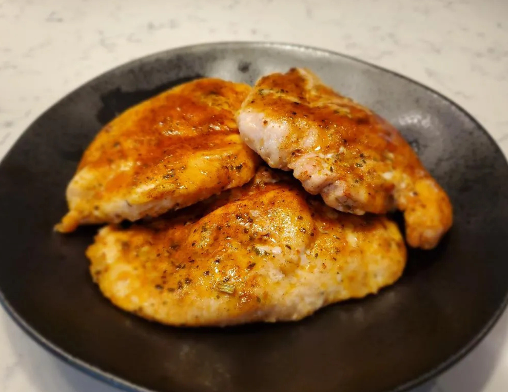 Three seasoned juicy chicken breasts on a black plate with a light background
